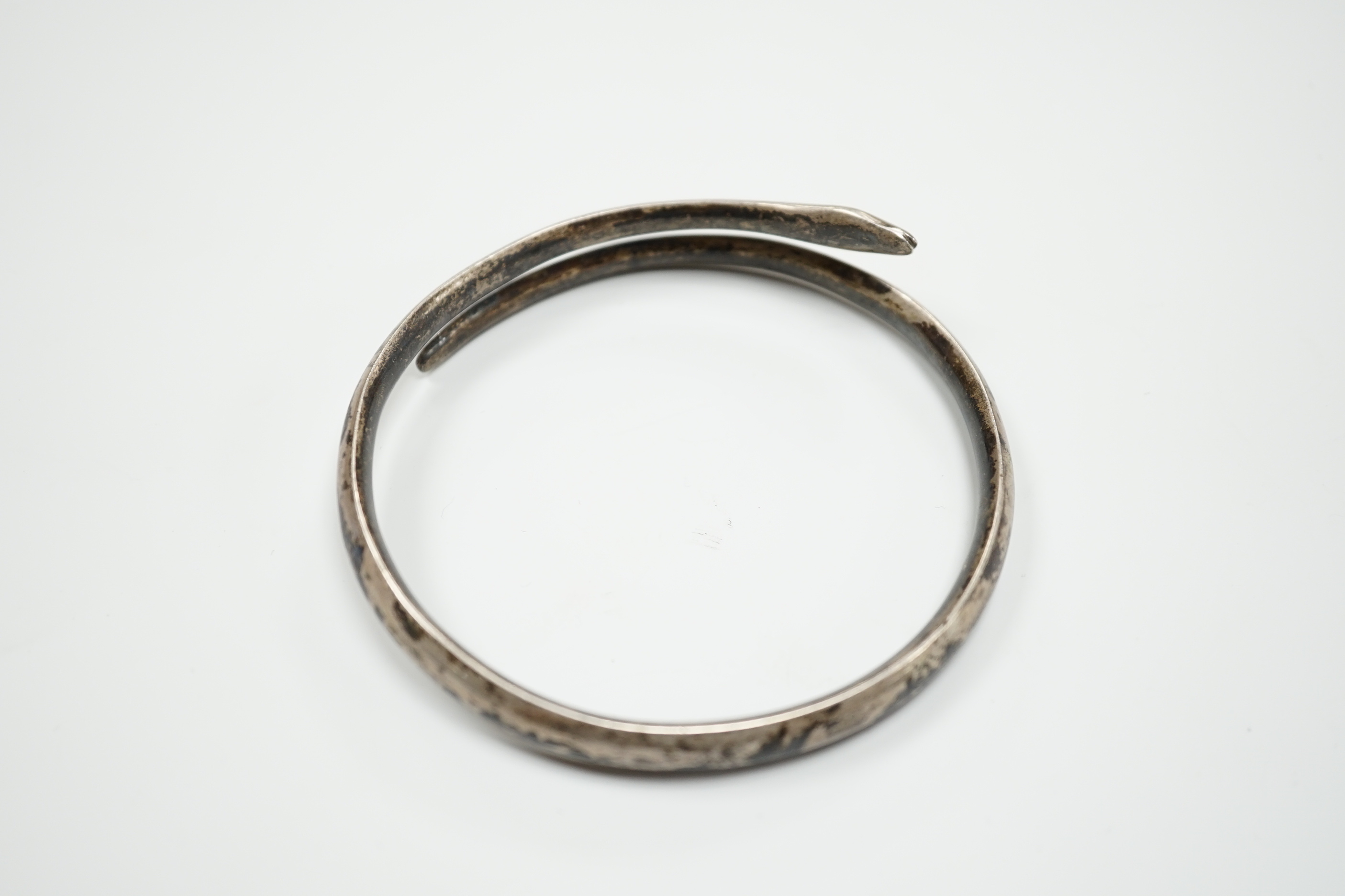 A white metal and niello serpent bangle, decorated with scene of a camel train.